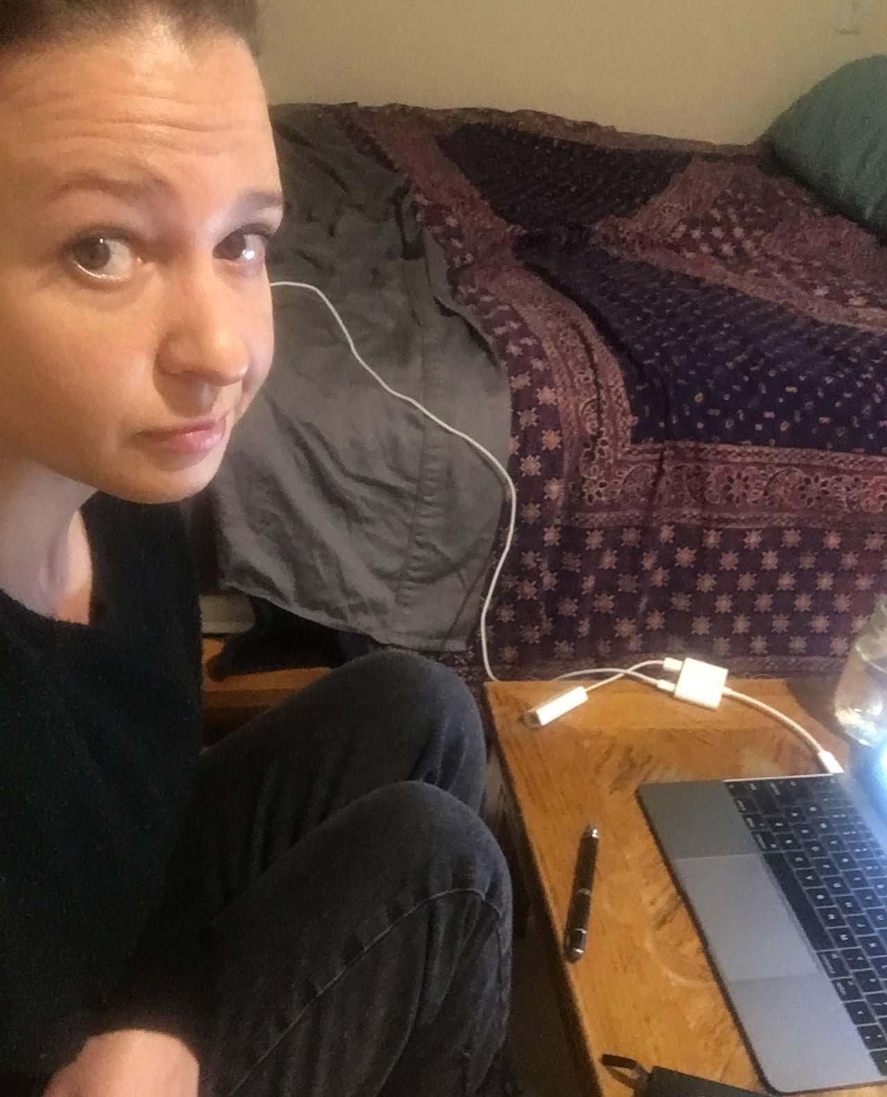 default-26 A woman poses for a selfie while sitting next to her laptop and bed.