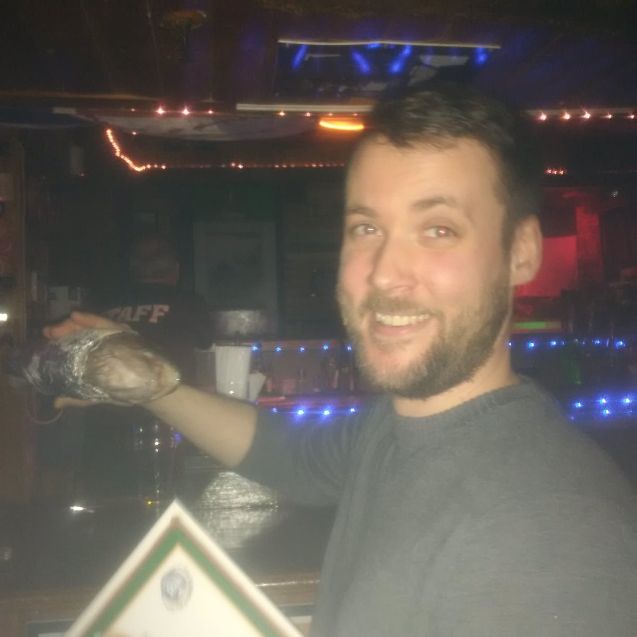 A man joyously holding a fish wrapped in foil in a bar.