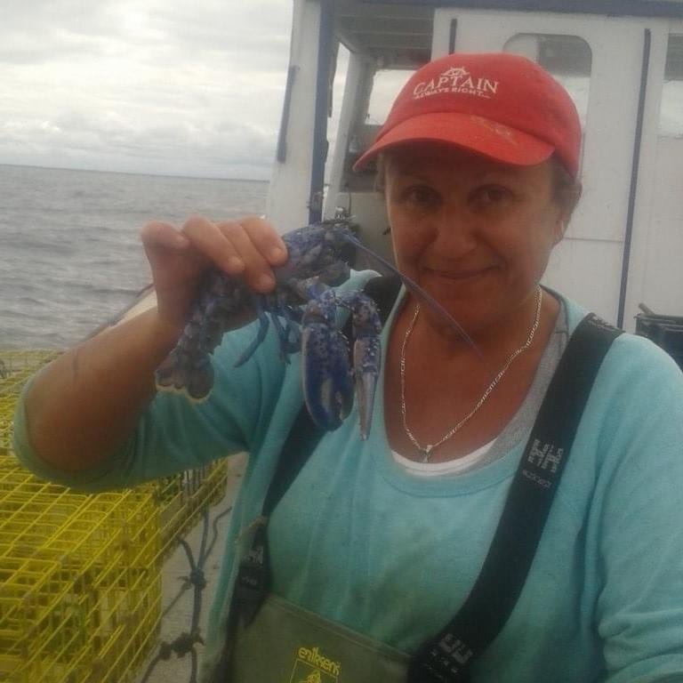 default-46 A woman in a red 'Captain' cap on a boat holding a blue lobster.
