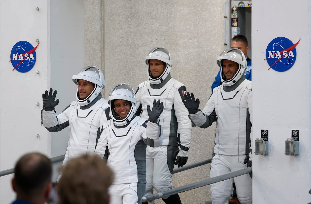 Four astronauts in white spacesuits and helmets.